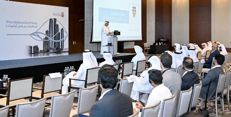 A speaker presenting at a conference to an audience, with many attendees dressed in traditional Gulf attire.