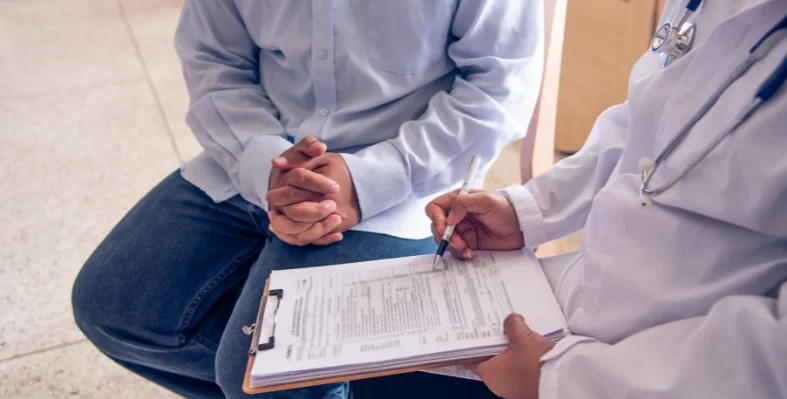A_doctor_writing_on_a_clipboard_as_they_sit_next_to_a_patient.