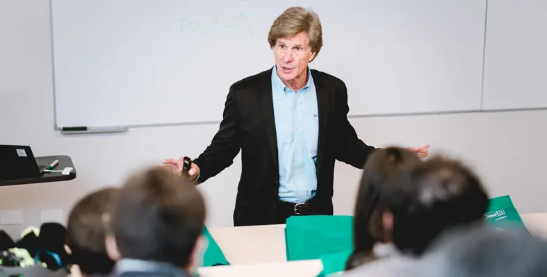 Man delivering class with students in the foreground and whiteboard in the background