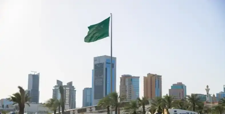 The Riyadh skyline with a Saudi Arabian flag waving in the foreground.