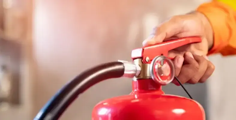 A worker in orange PPE opening the valve on a fire extinguisher.
