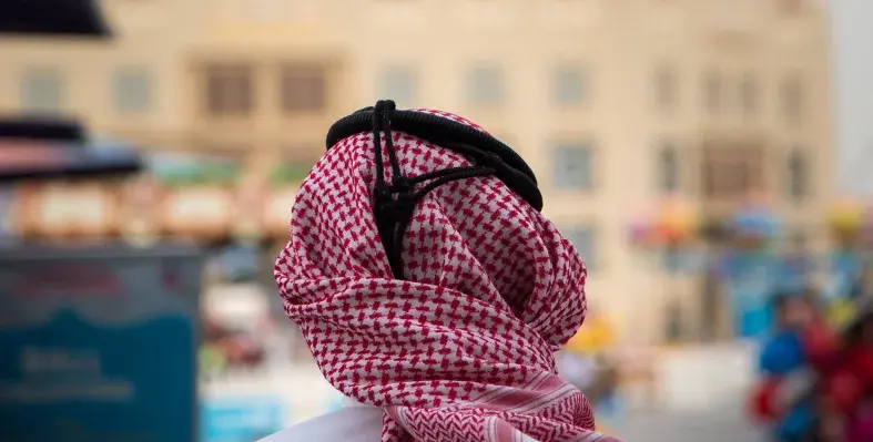 View from behind of a man in cultural headdress facing towards al Fanar in Doha, Qatar.