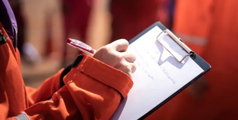 A_person_in_orange_PPE_writing_on_a_clipboard.