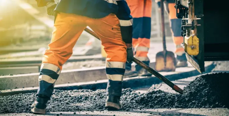 A worker shovelling tarmac for a rail construction project in the sunlight.