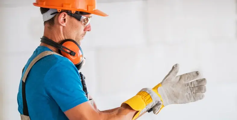 A worker in PPE putting on safety gloves.